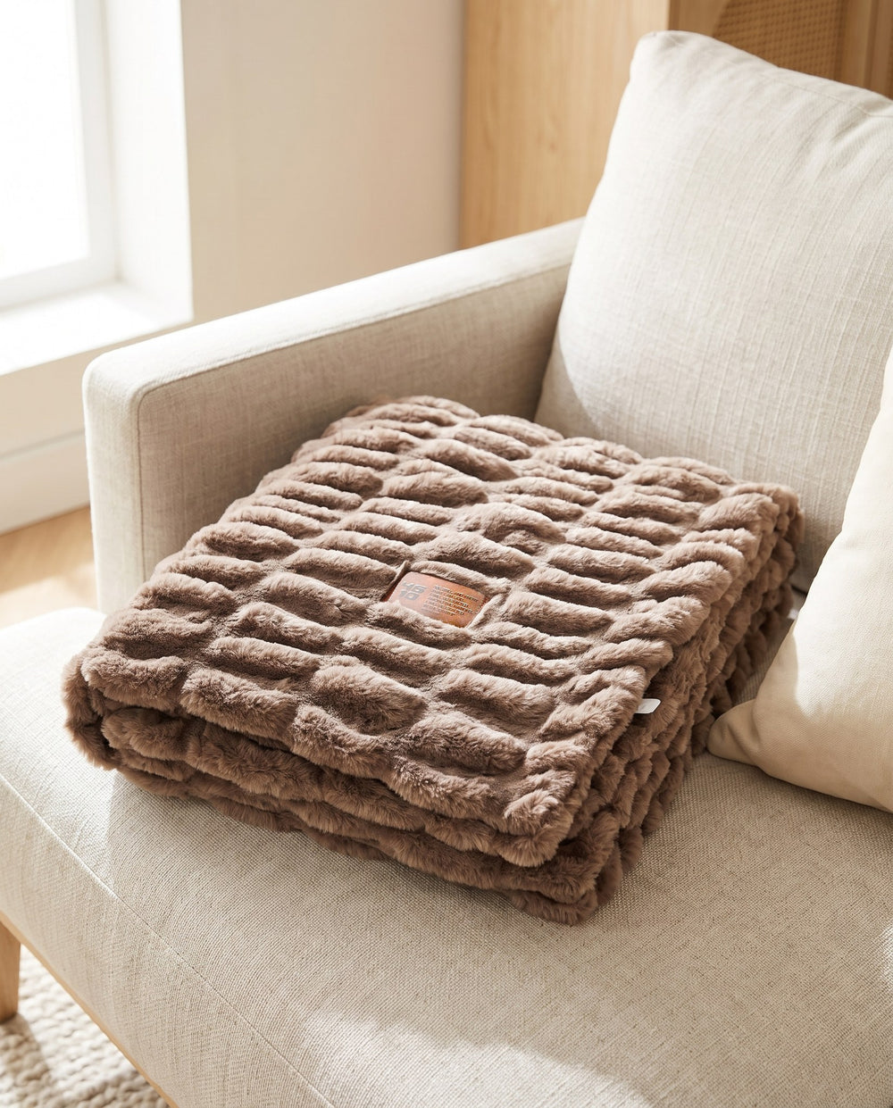 Be Still Blanket folded on a sofa, showing the debossed leather patch with the 46/10 logo and Psalm 46:10