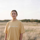 Model wearing the butter yellow Chosen Pursued Loved tee in an open field at golden hour