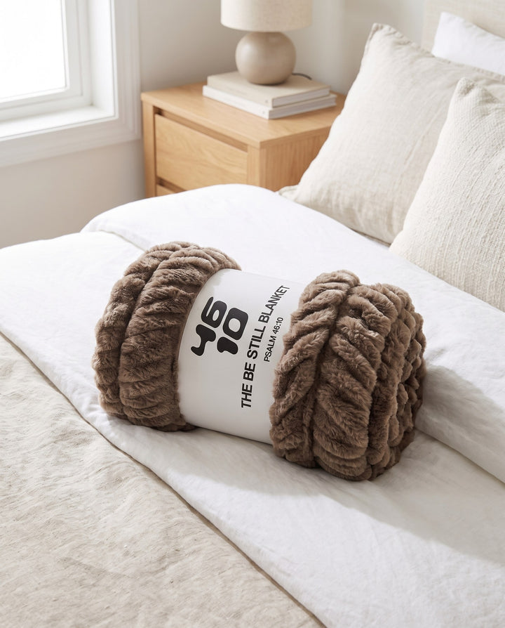 The Be Still Blanket rolled in its paper band on a bed