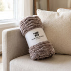 The Be Still Blanket rolled in its white paper band printed with the 46/10 logo and Psalm 46:10, on a linen sofa