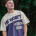 Man wearing streetwear tee with 'He Won't Give Up On Me' text, outdoor nature background