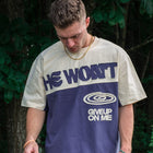 Man wearing a streetwear tee with 'He Won't Give Up On Me' text, outdoors in nature.