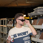 Man wearing 'He Won't Give Up On Me' Christian streetwear tee, holding coffee in warehouse