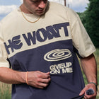 Man wearing colorblock streetwear tee with 'He Won't Give Up On Me' text outdoors